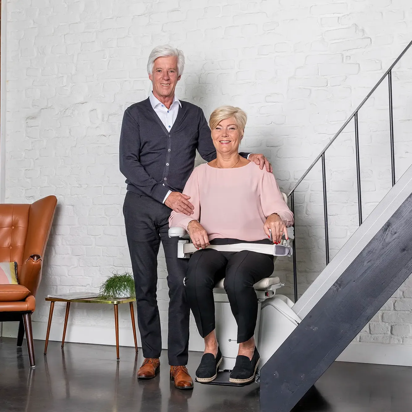Treppenlift von der Firma Handicare. Eine Frau sitzt im Treppenlift und Ihr Mann steht neben ihr. Niedersachsen Lifte führt Maschinen von Handicare.