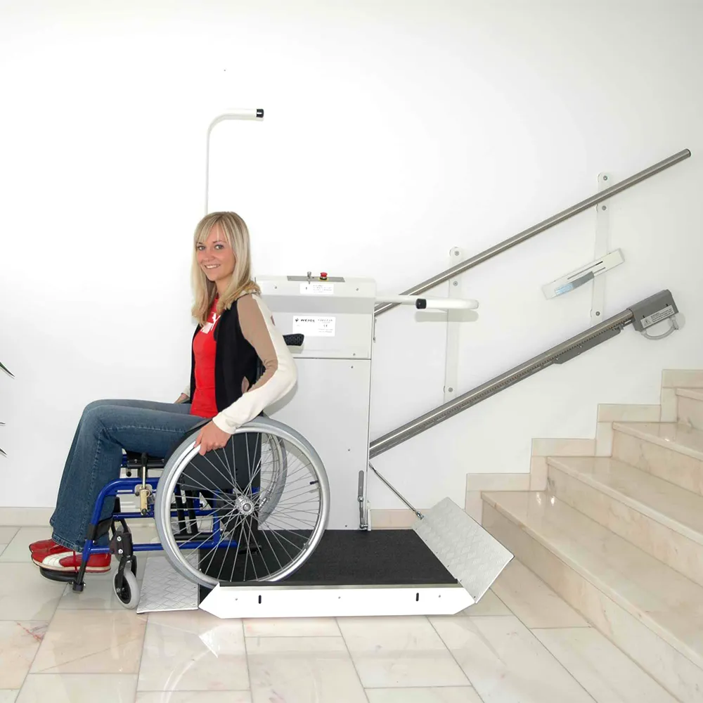 Eine Frau sitzt im Rollstuhl auf einem Plattformlift und zeigt die Funktionen